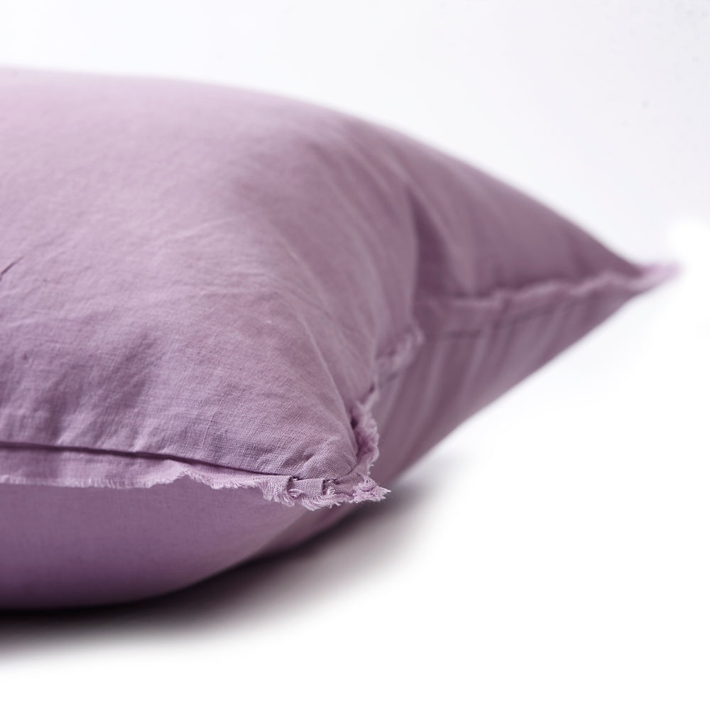 Soft jacaranda bedhead cushion in stonewashed French flax linen, with hand-tufted edges, offering a delicate, floral-inspired hue and sophisticated charm.